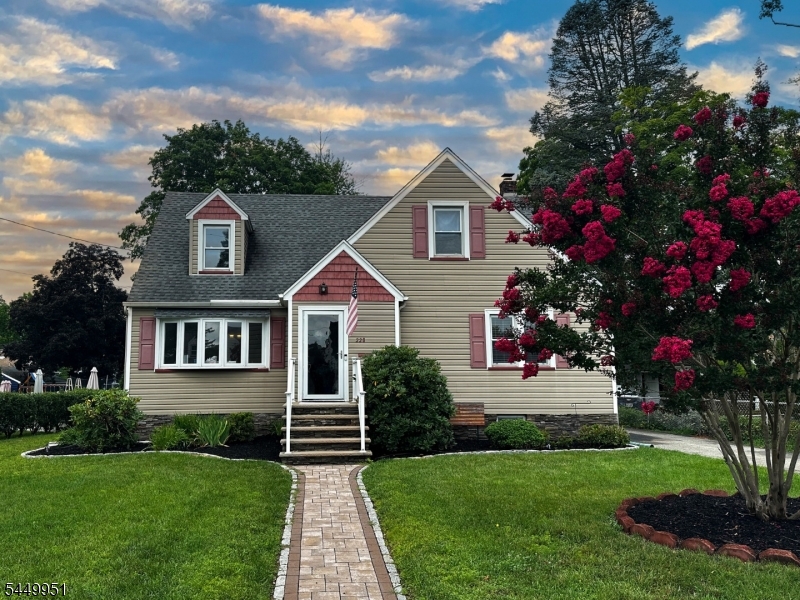 Inviting front exterior featuring a paver walkway, manicured lawn, mature landscaping, and a beautiful flowering tree framing the homeÃ¢??s entrance.