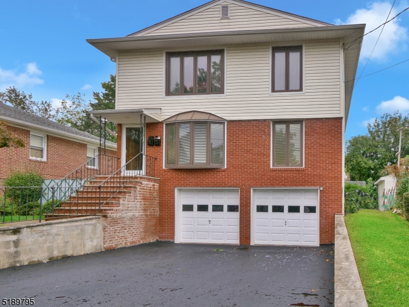 Multi-level brick and siding exterior featuring a two-car garage and an expansive paved driveway.