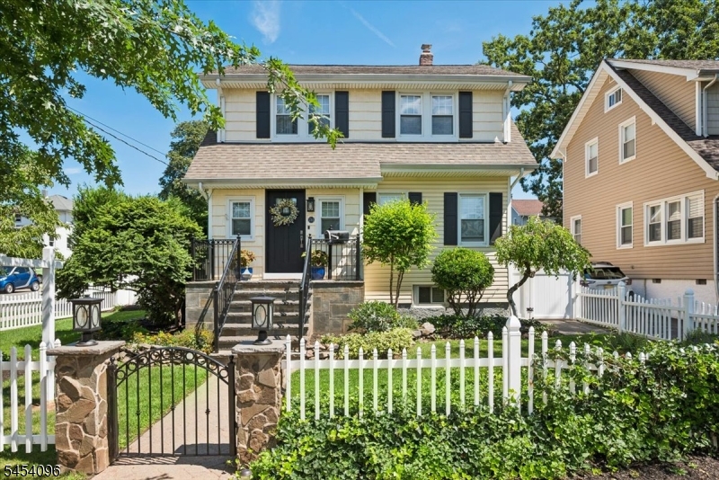 Charming curb appeal with a beautifully landscaped front yard, classic white picket fence, and stone columns with decorative lighting framing the entry gate.