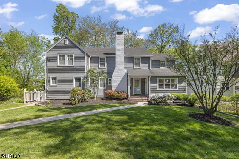 Classic exterior with attractive gray siding, crisp white trim, a striking chimney, and beautifully manicured landscaping.