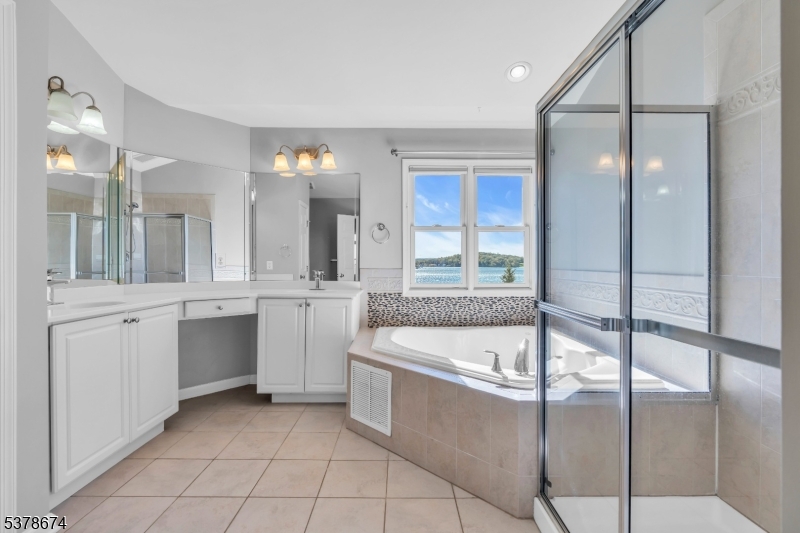 Primary bath Soaking tub, separate glass shower and two double sink vanities all with the backdrop of lake views.