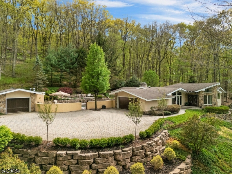 Winding drive to upper paver driveway. Detached garage on the left provides space for more cars and a workshop area and houses the pool equipment in a separate section.