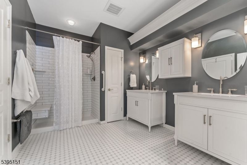 Beautifully updated ensuite bath features sconce lighting, dual stylish vanities w rectangular sinks set in quartz tops,oversized shower in subway tile surround w bench & grab bars, private water closet, mosaic tile floor, linen closet & large WI closet.
