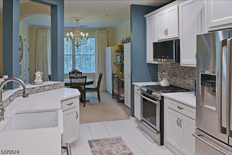 Beautifully updated chef's kitchen with all stainless steel appliances, quartz countertops, glass-tile backsplash. View of breakfast room in background.