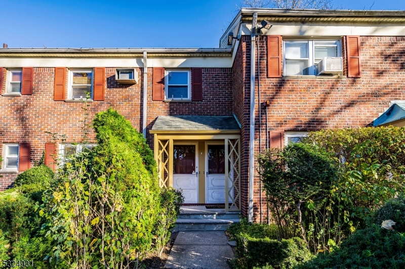 Charming brick facade with under a covered entry. Accented with shutters and surrounded by lush greenery and mature shrubs along the walkway.